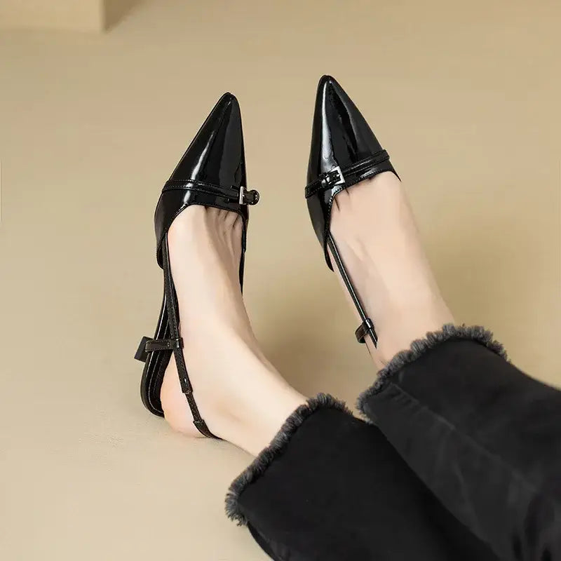 Black patent slingback heels with a pointed toe and buckle detail. Women's dress shoes.