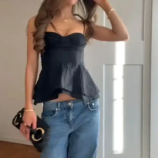 Woman wearing a black sexy bow backless slip top paired with blue jeans and holding a black purse