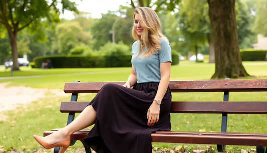 Woman wearing a black midi dress and blue top sitting on a park bench for midi dress styling tips for special occasions