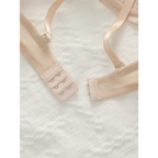 Beige adjustable shoulder strap lingerie bra with hook and eye closure on white textured fabric