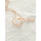 Beige adjustable shoulder strap lingerie bra strap with slider on a white textured fabric background