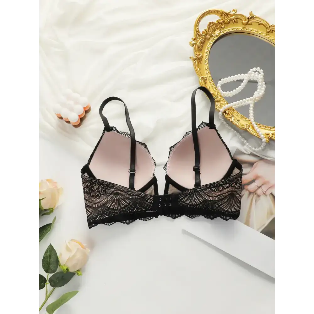 Black adjustable strap lace bra for women with floral lace design laid on white fabric background