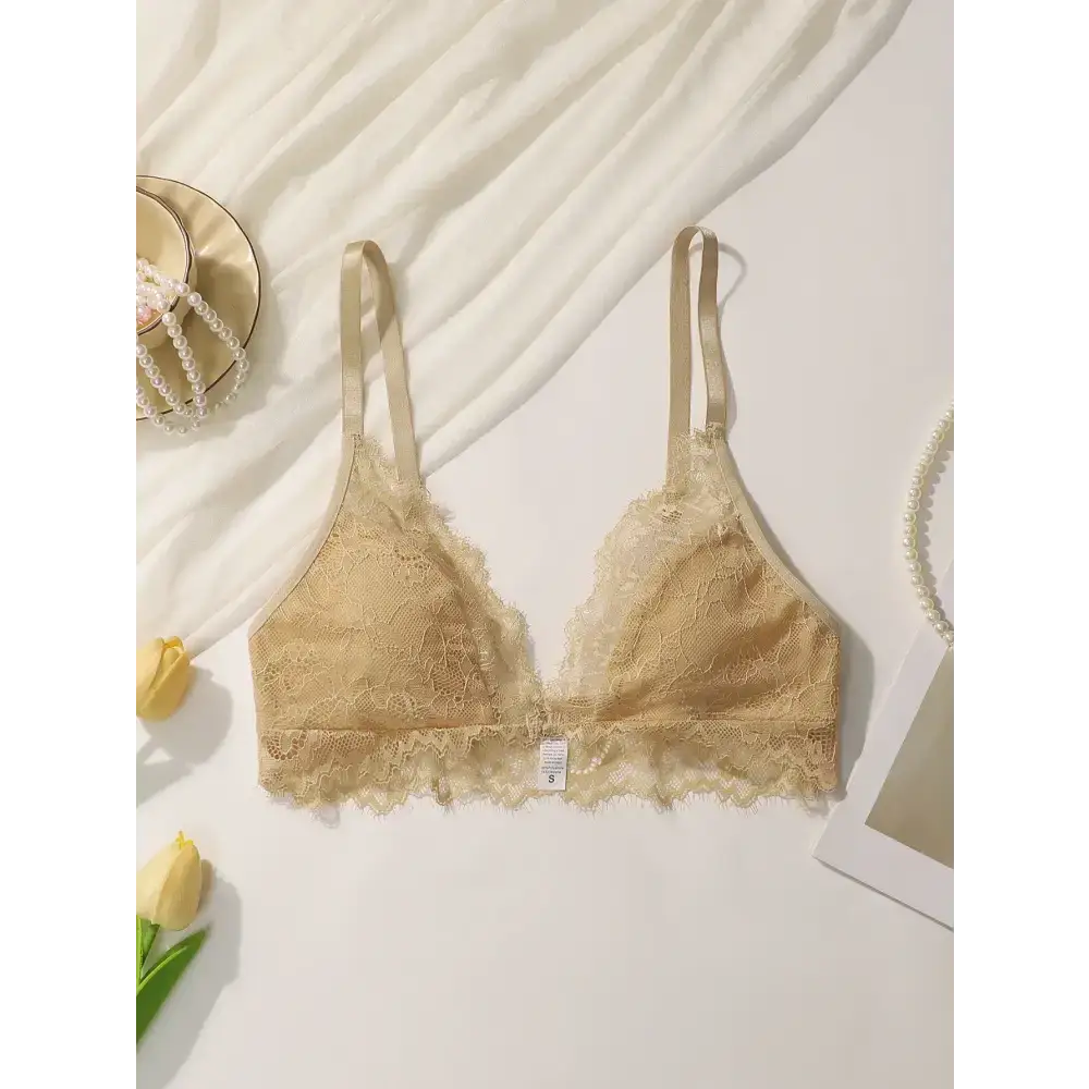 Beige lace adjustable strap wireless bra from The Lady's Haven Boutique laid flat with decorative flowers and accessories