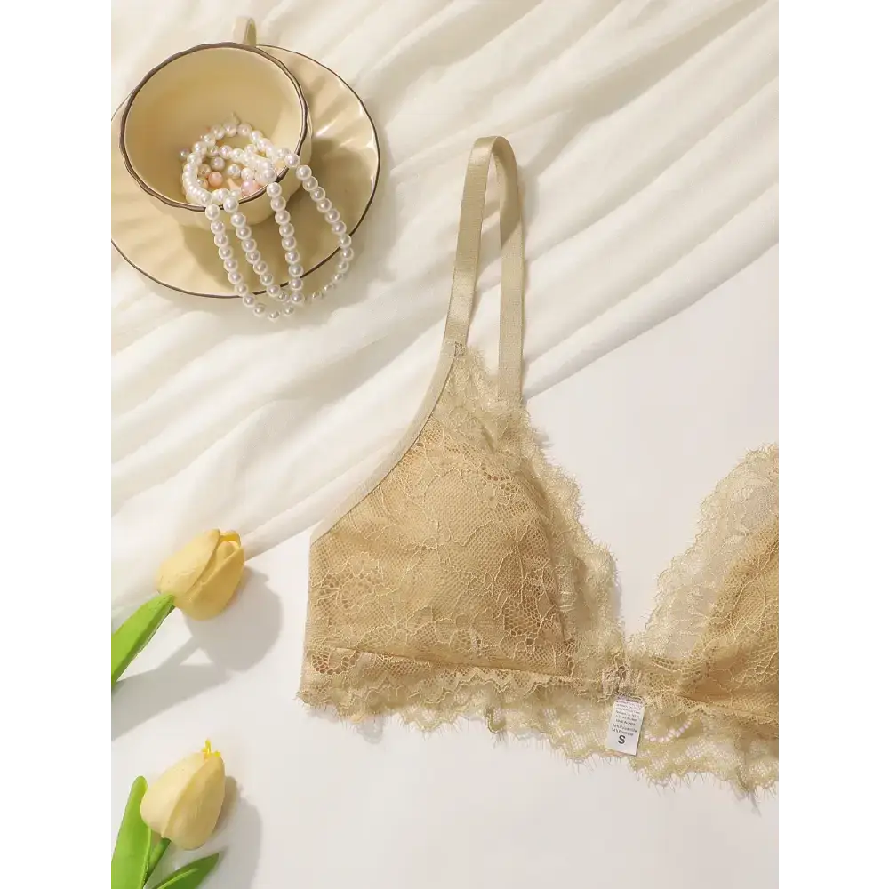 Beige lace adjustable strap wireless bra laid flat with pearl necklace and yellow tulips