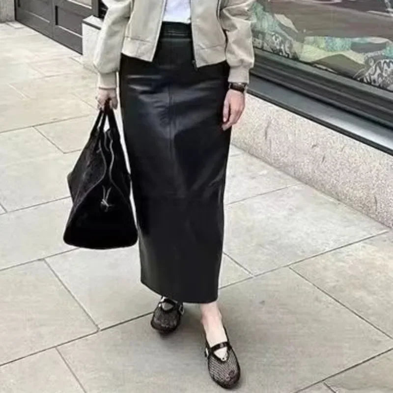 Woman wearing black mesh fashion sandals paired with a black leather skirt and beige jacket carrying a black bag