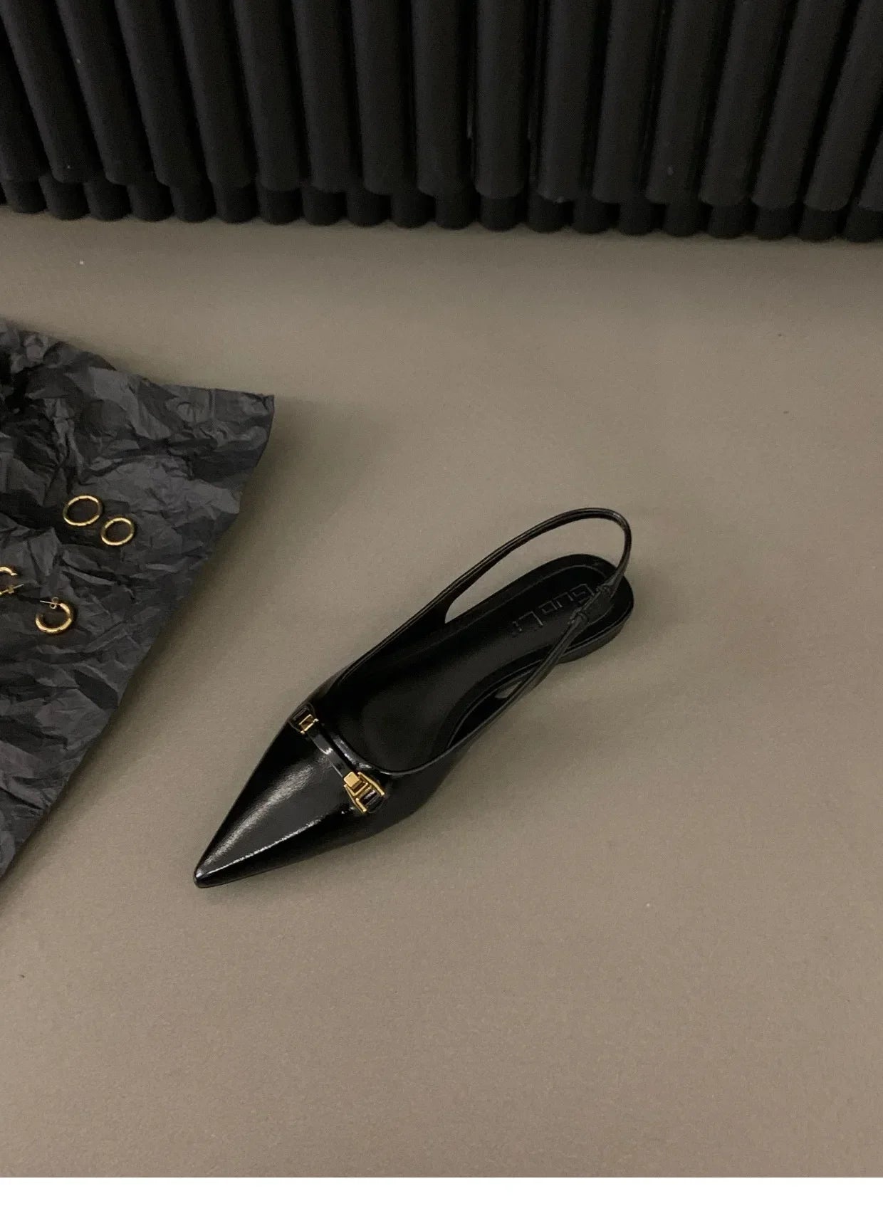 Black leather pointed toe mid heel sandals with gold buckle detail on beige surface