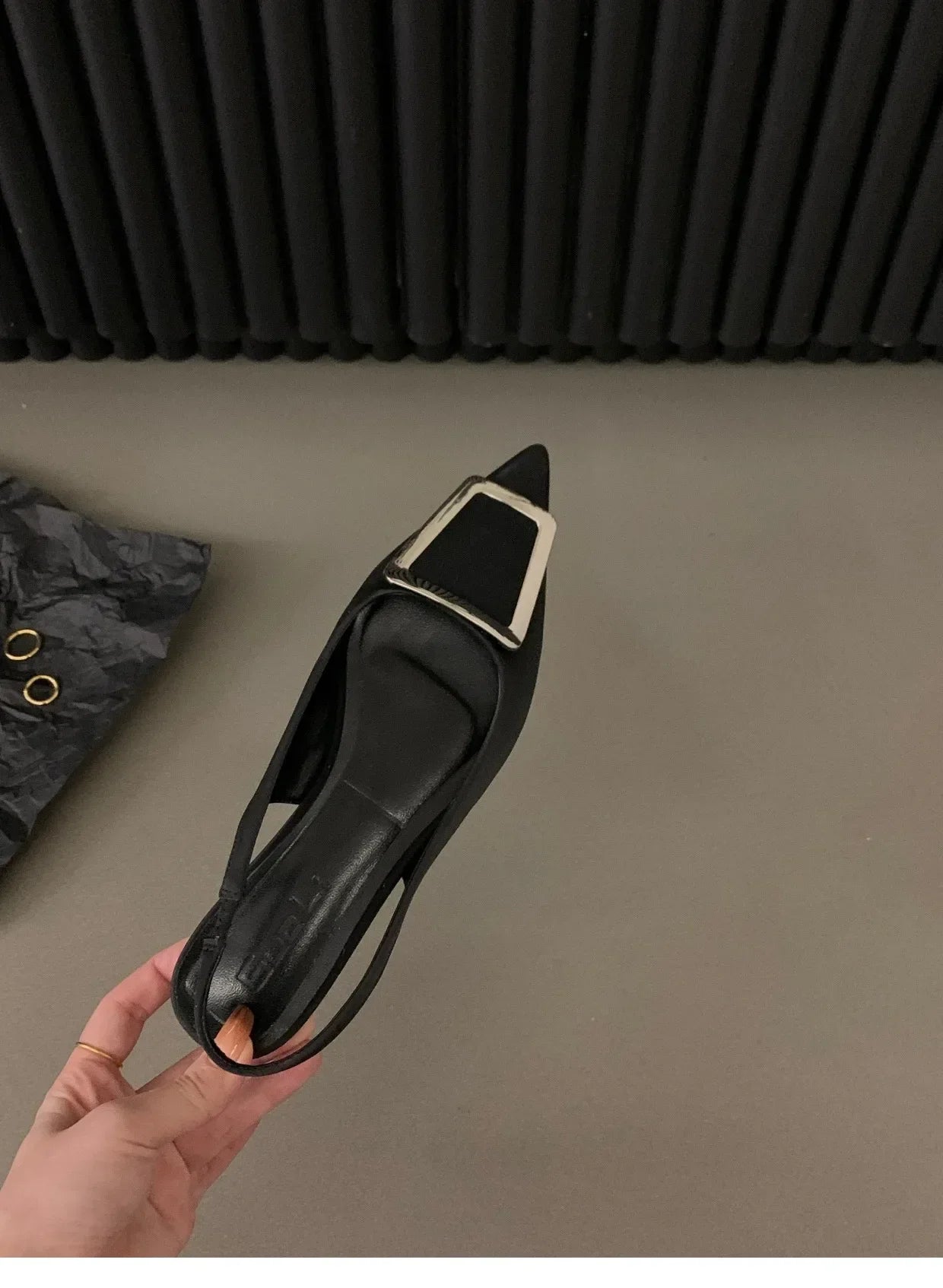 Black pointed toe mid heel sandals with a decorative buckle held in hand against gray background