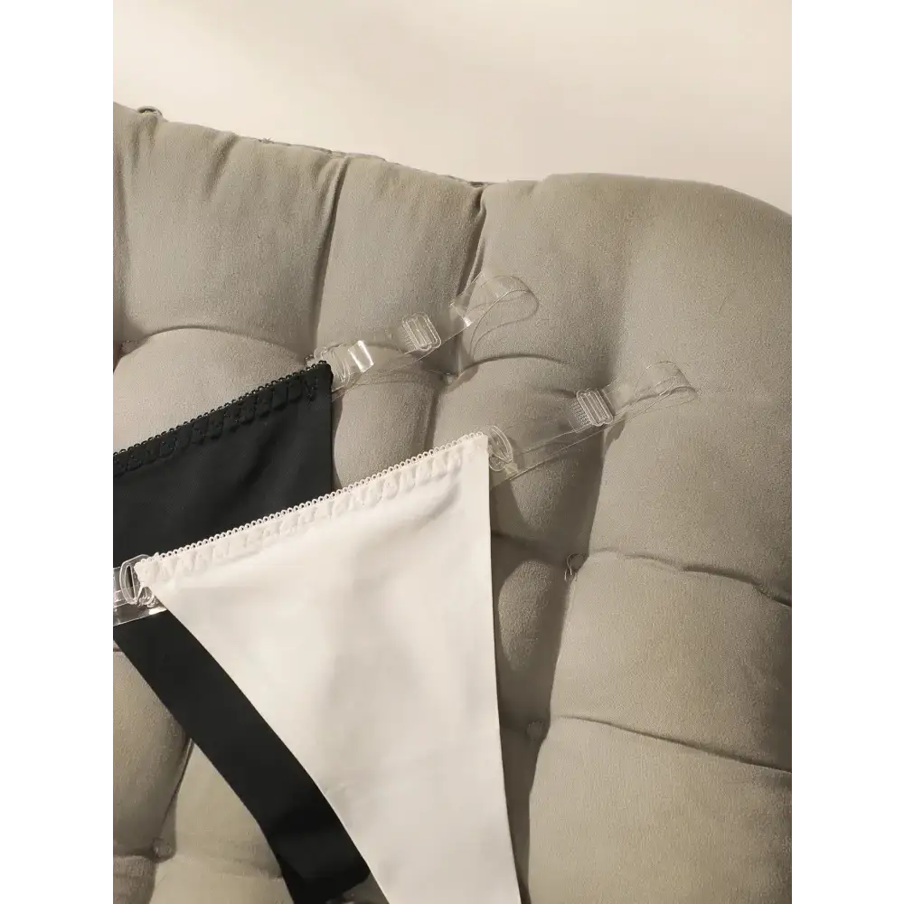 Black and white seamless thong underwear with clear adjustable straps displayed on a beige couch