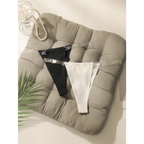 Seamless thong underwear in black and white with clear straps displayed on a cushioned gray pad