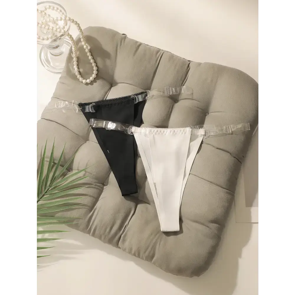 Seamless thong underwear in black and white with clear straps displayed on a cushioned gray pad