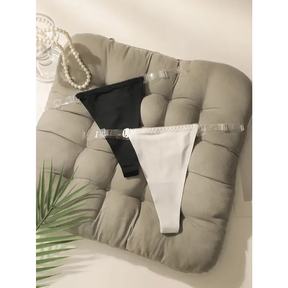 Black and white seamless thong underwear with clear straps displayed on a cushioned chair