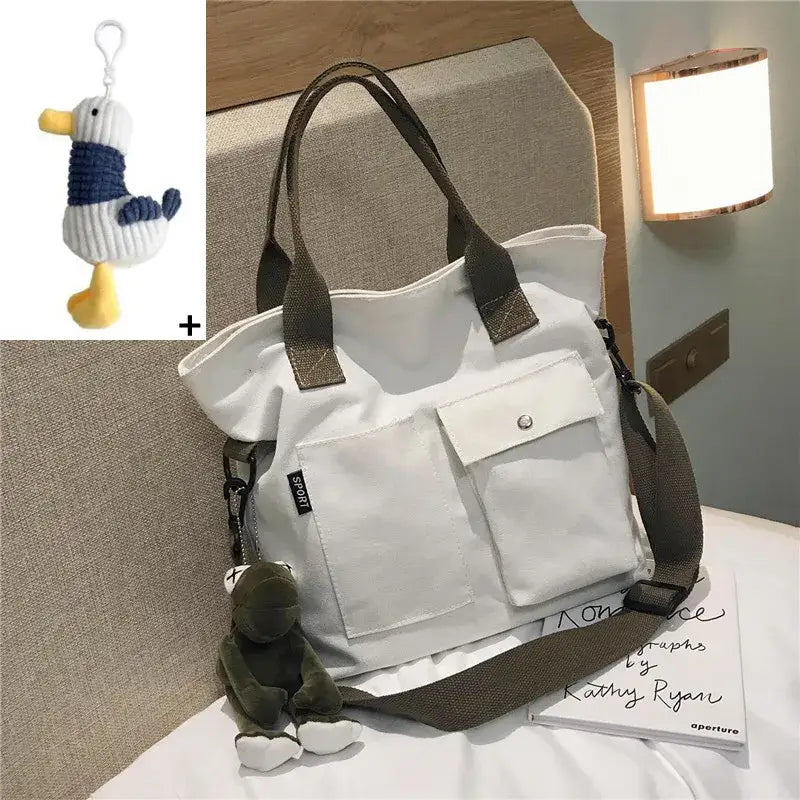 Casual canvas tote bag for women with two front pockets and detachable charm on a bed