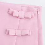 Close-up of pink fabric with decorative bows and zipper detail on casual mid waist short skirt