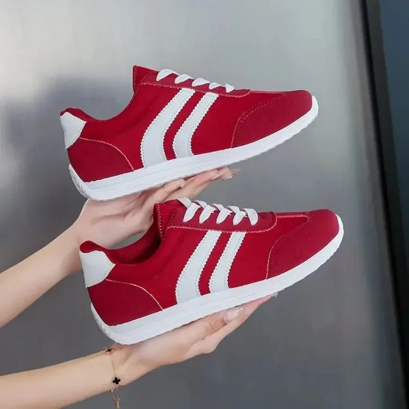 Red casual slip on sneakers with white stripes and laces held in hands against gray background