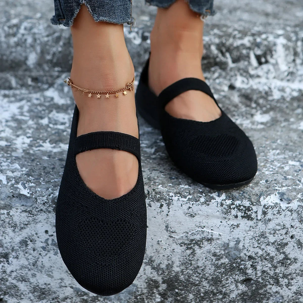 Black comfortable slip-on shoes with strap worn with ankle bracelet and rolled jeans on stone surface