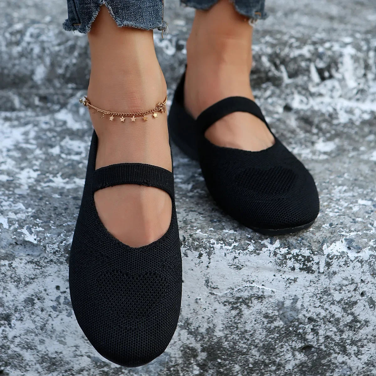Black comfortable slip-on shoes with strap worn with ankle bracelet and rolled jeans on stone surface