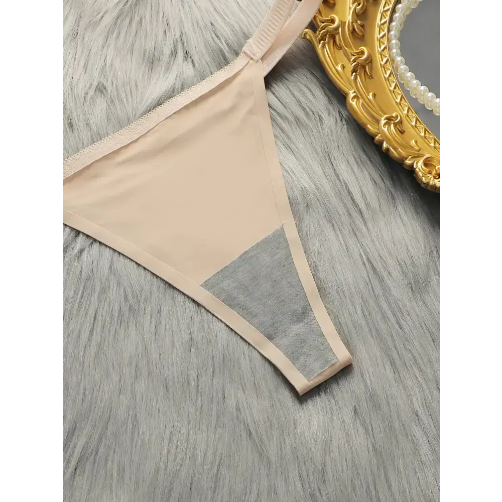 Beige comfortable steel ring lingerie for women thong laid on gray fur background with golden ornate mirror