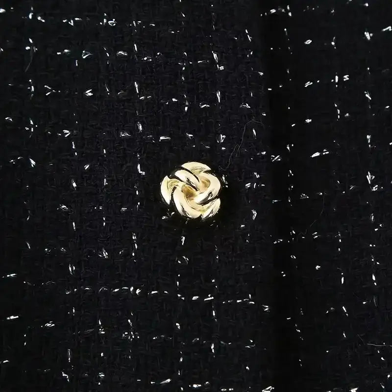 Close-up of black textured fabric with gold button detail from cropped vest and high waist shorts set