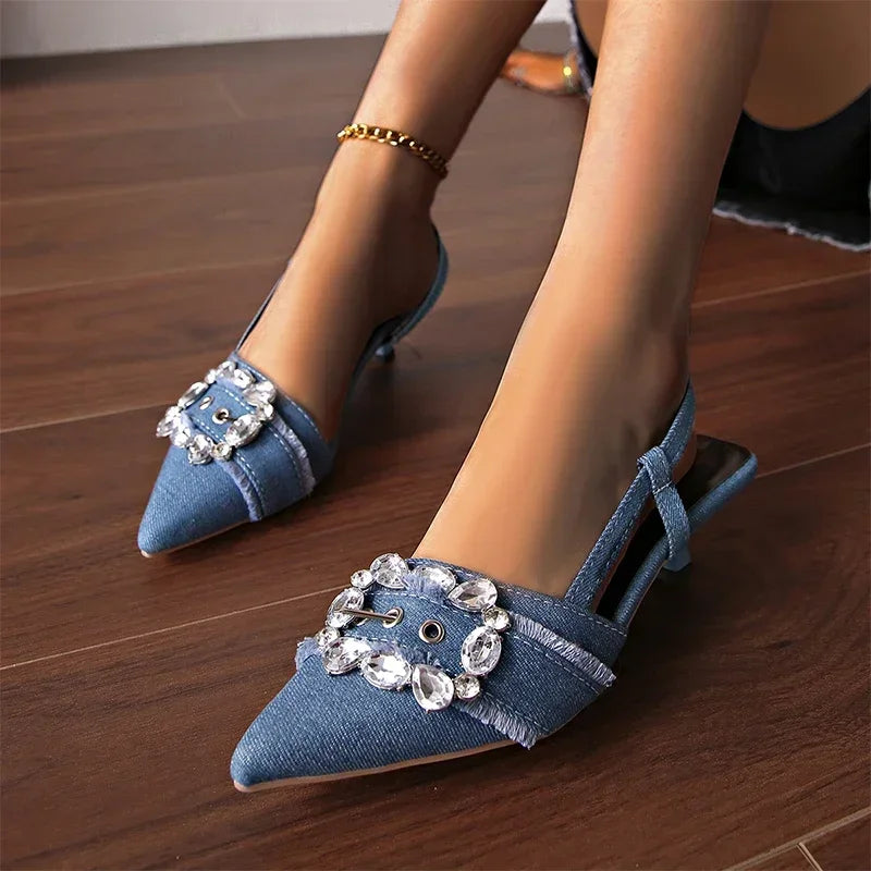 Blue denim pointed toe stiletto sandals with decorative rhinestone buckle on wooden floor