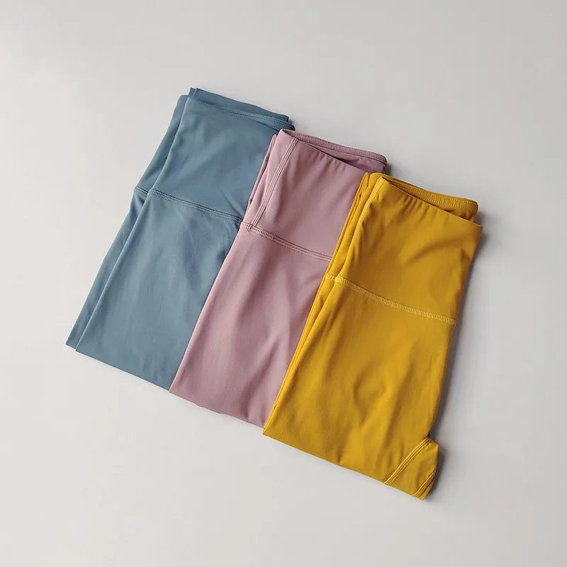 Three pairs of elastic fitness leggings for women in blue, pink, and yellow colors on a neutral background
