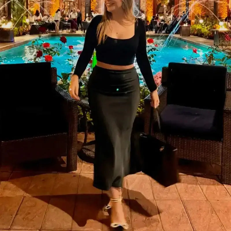Woman wearing a black ladies evening skirt and matching crop top by the poolside at night