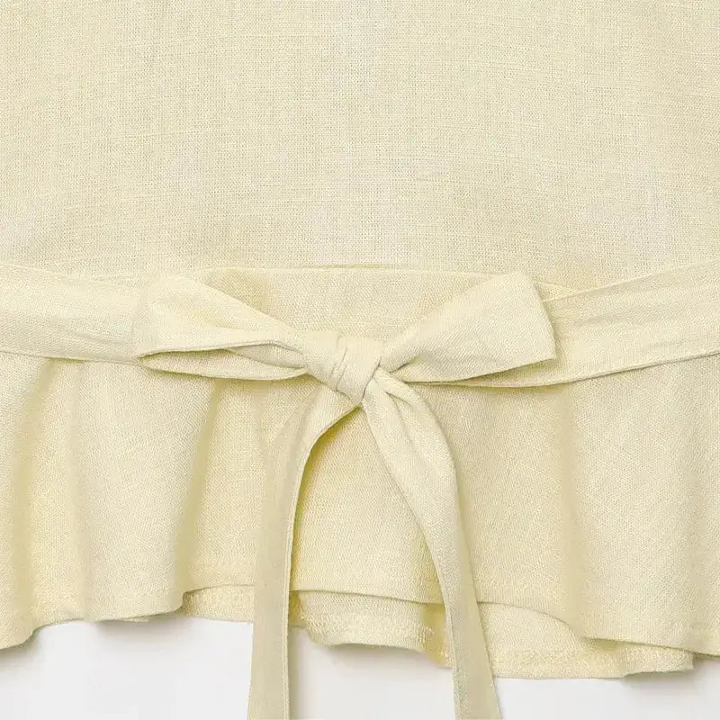 Close-up of cream fabric texture and tied waist detail on short sleeve blouse and pant set