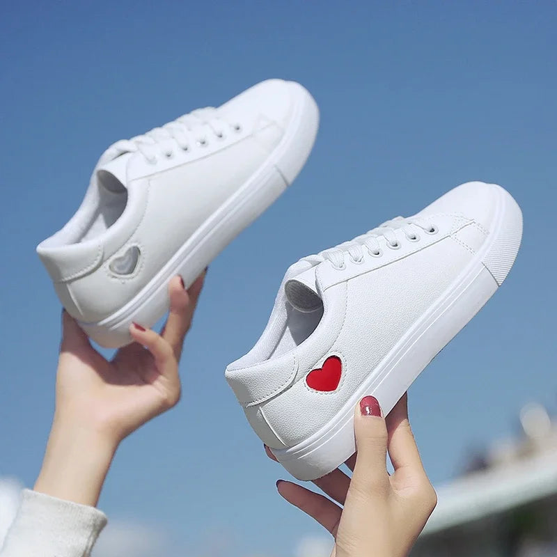 White flower design running shoes for ladies with red and silver heart accents held against blue sky