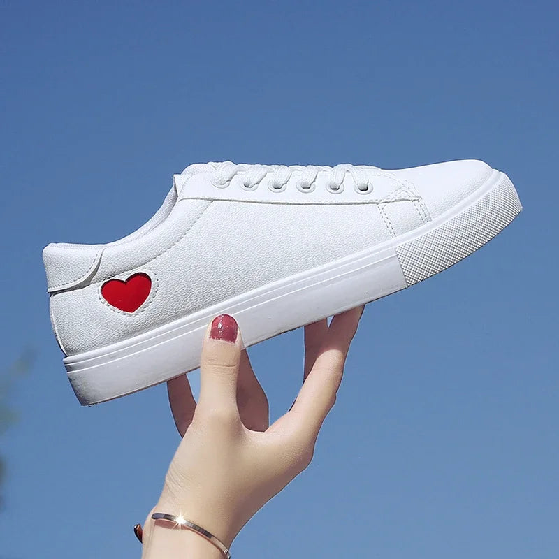 White casual sneaker with red heart design held against blue sky, flower design running shoes for ladies
