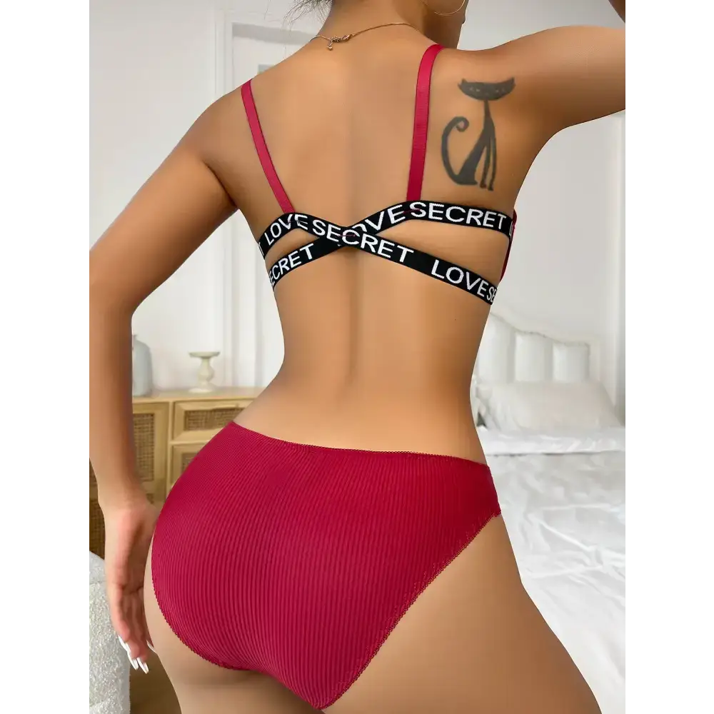 Back view of woman wearing red front button bralette and panties with black elastic straps in a bedroom