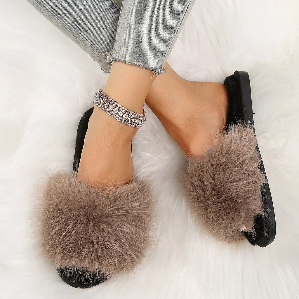 Brown fuzzy flat slide slippers with black soles worn with light blue jeans on white background