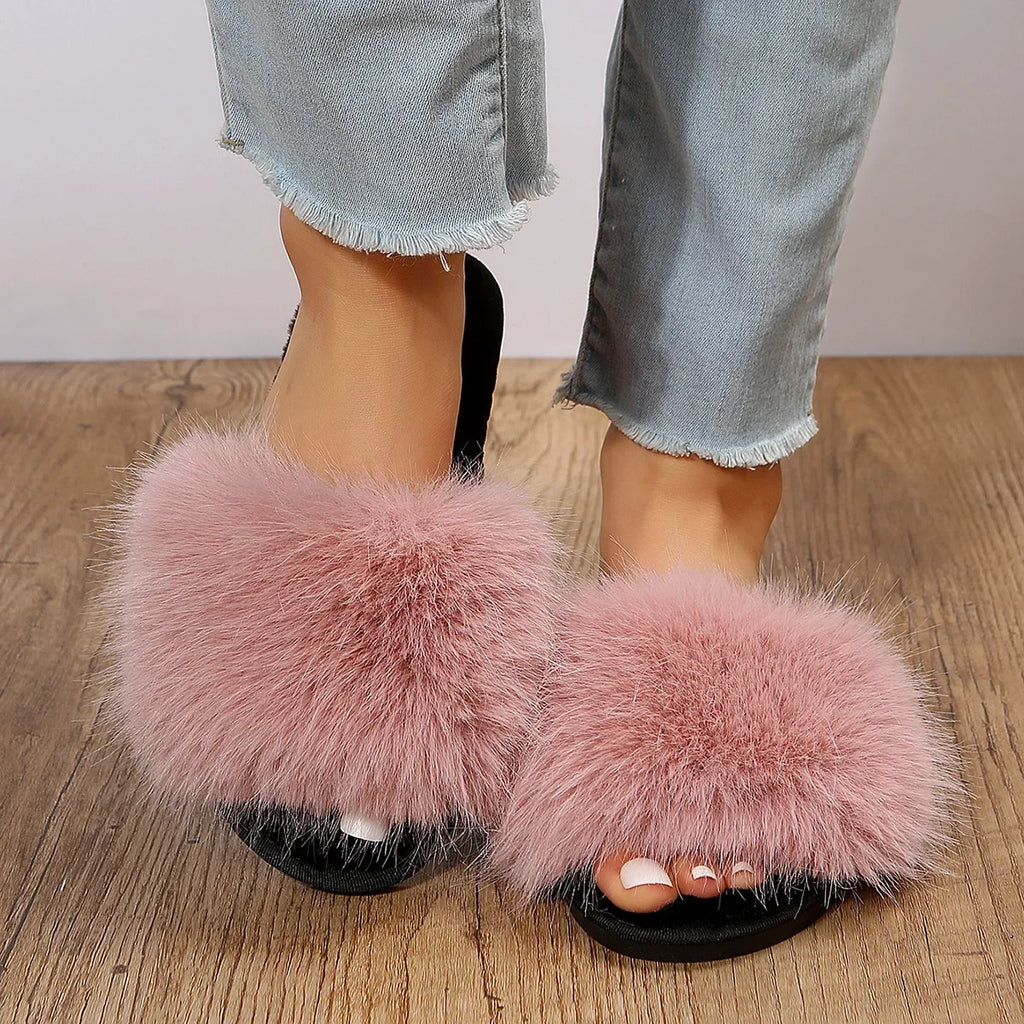 Pink fuzzy flat slide slippers with soft fur strap worn with cropped light blue jeans on wooden floor
