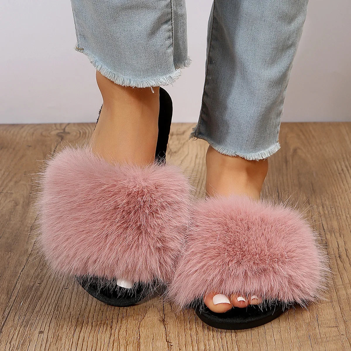 Pink fuzzy flat slide slippers with soft fur strap worn with cropped light blue jeans on wooden floor