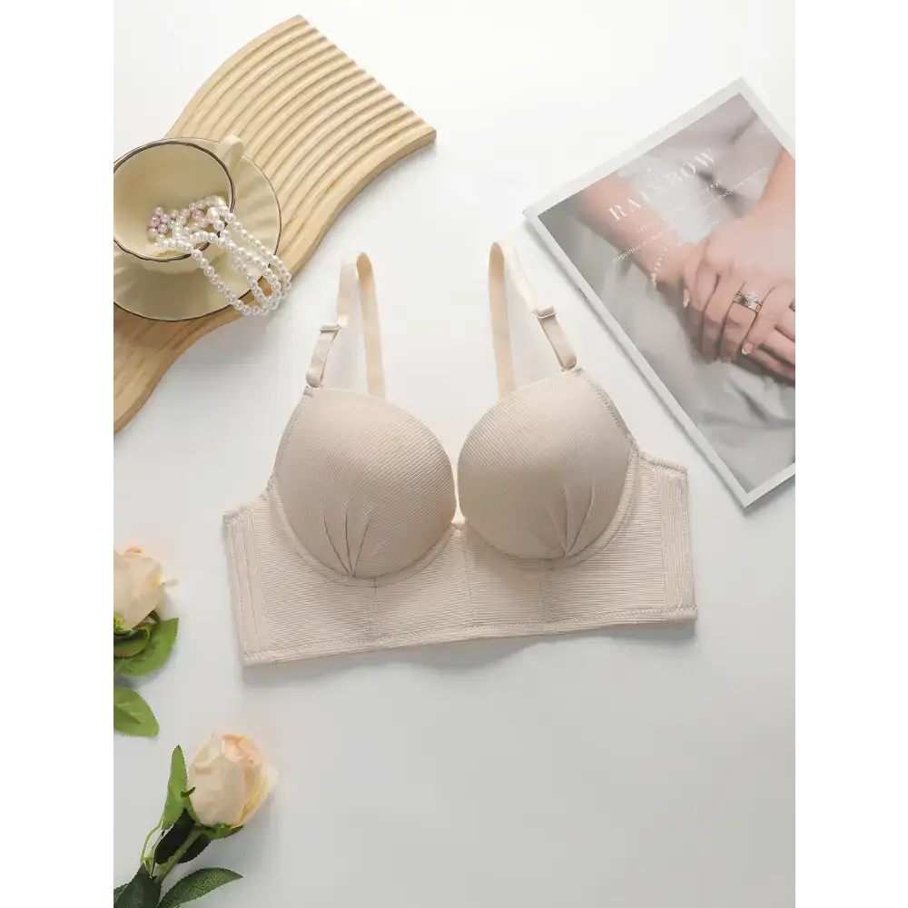 Beige gathering push up bra for ladies displayed with magazine and pearls on white surface