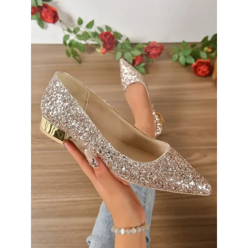 Glittery flats for parties with pointed toe and gold heel held by a hand over wooden floor