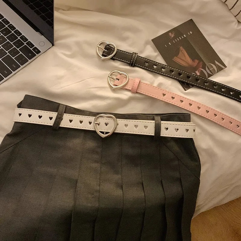 Heart buckle waist belt in black, pink, and white designs laid on a skirt for stylish outfit inspiration