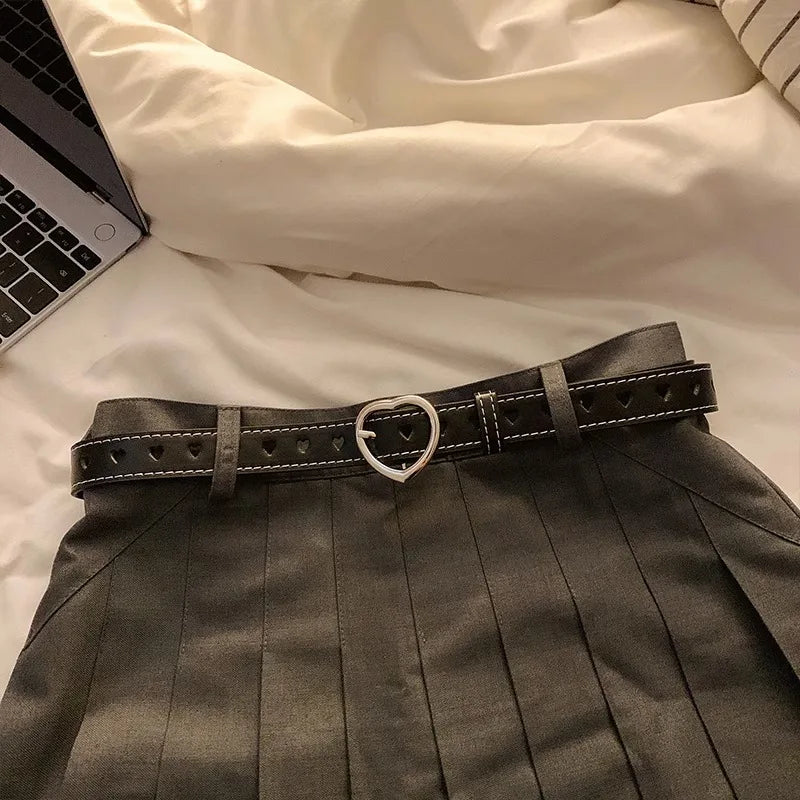 Stylish heart buckle waist belt in black with a chic pleated skirt on a bed