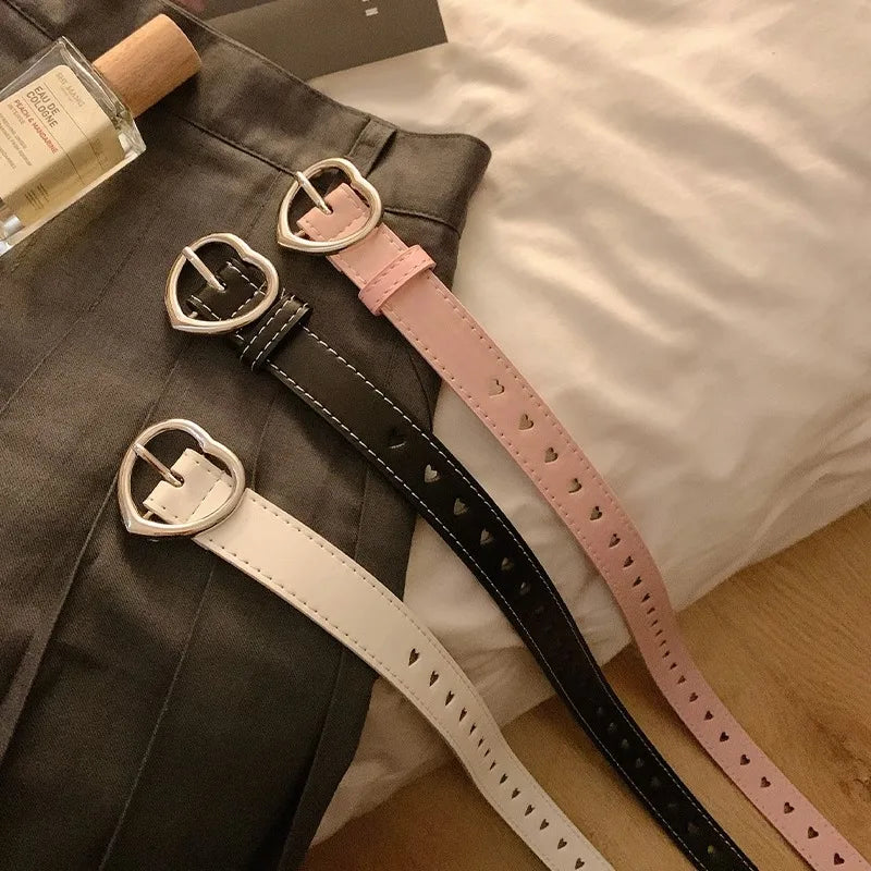 Heart buckle waist belt in black, white, and pink on a flat surface for stylish outfit accessorizing