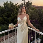 Woman wearing a sleeveless satin formal dress in cream with thin straps posing outdoors at sunset