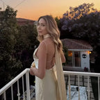 Woman wearing a sleeveless satin formal dress standing on a balcony during sunset