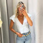 Woman wearing a white short sleeve blouse and pant set with a deep V neckline and ruffle details