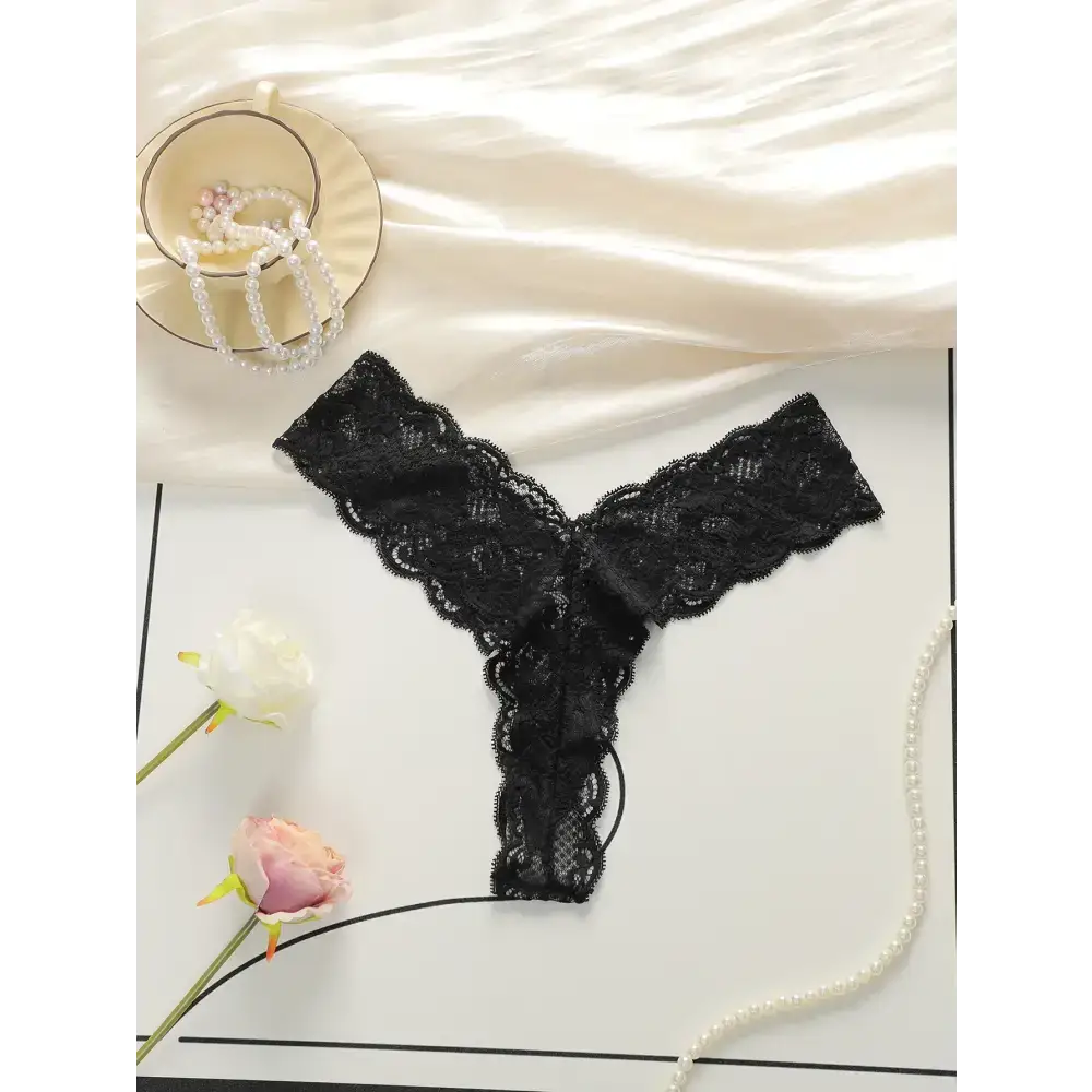 Black lace thong underwear for women displayed with pearls and flowers on white background