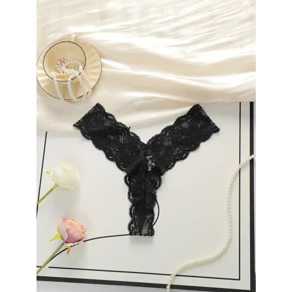 Black lace thong underwear for women displayed flat with pearls and flowers on a white surface