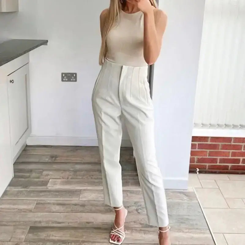 Woman wearing elegant slim fit pencil trousers in white paired with a sleeveless beige top and heels