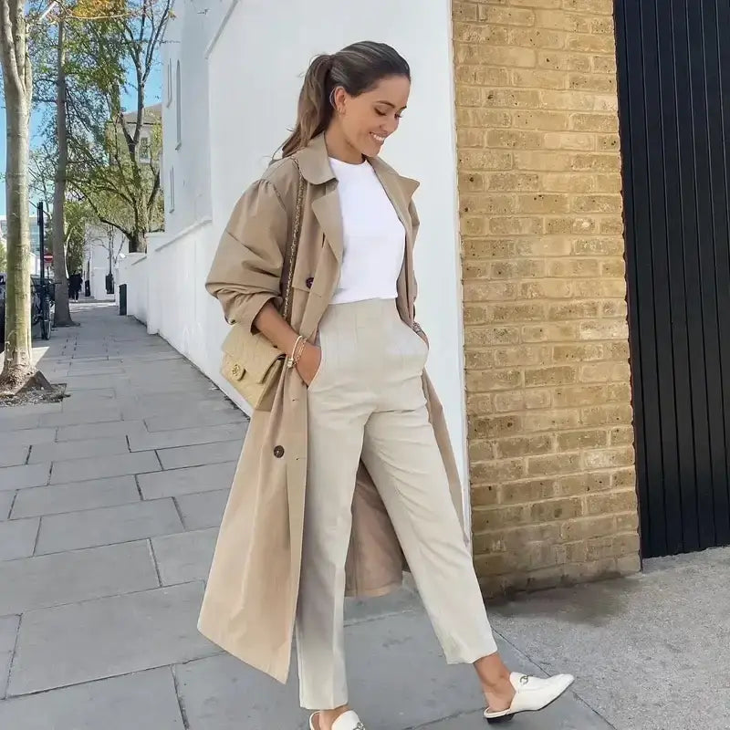 Woman wearing elegant slim fit pencil trousers paired with white top and beige trench coat outdoors