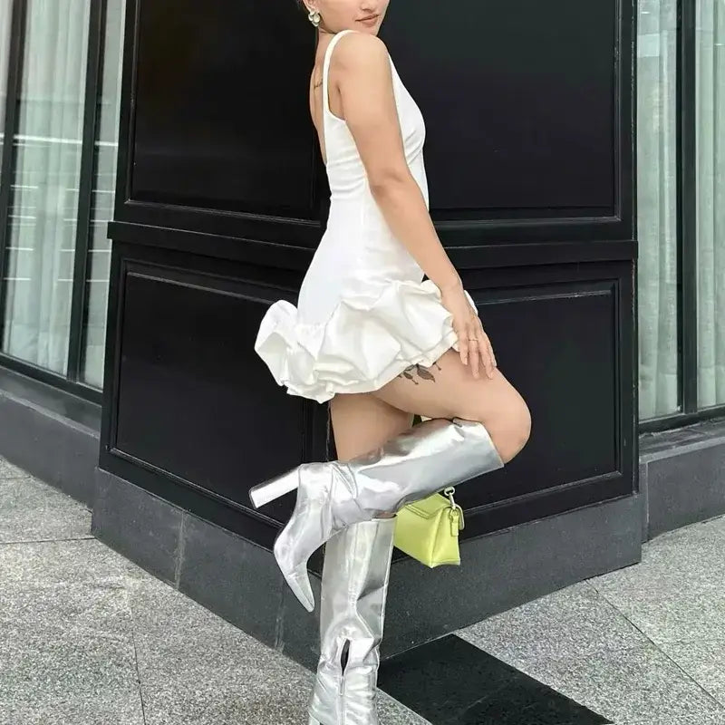 Woman wearing white summer party mini dress with ruffled hem and silver knee-high boots