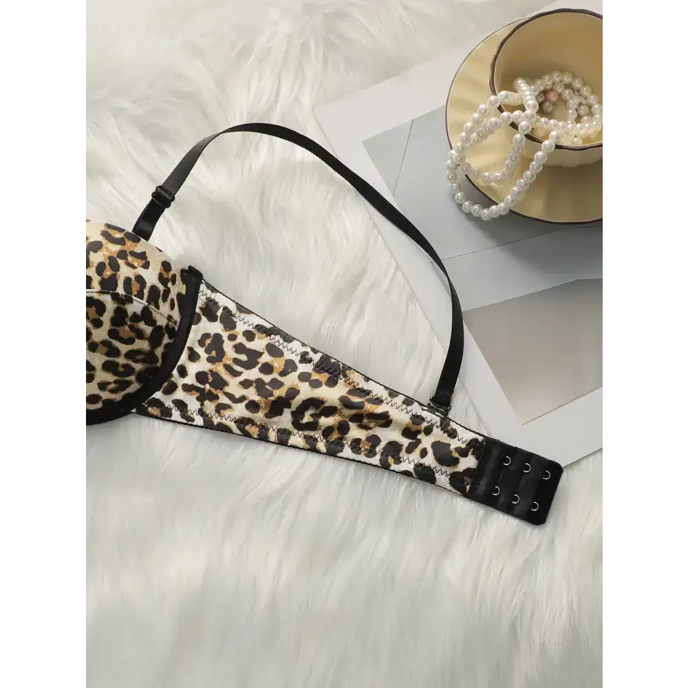 Leopard print push up bra with adjustable black straps laid on white fur next to pearl necklace
