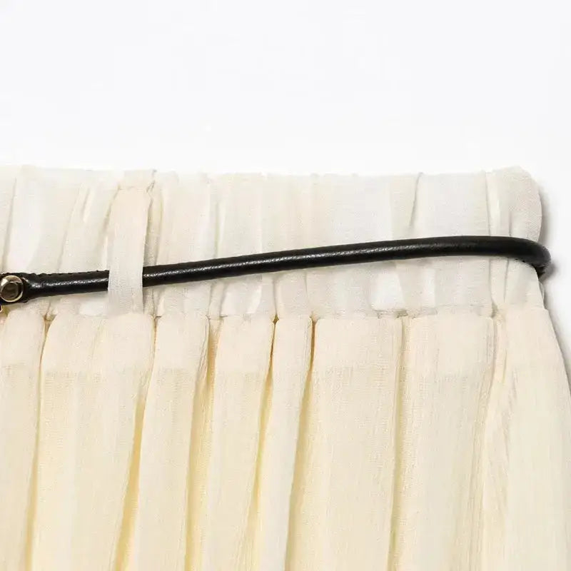 Close-up of a cream pleated chiffon midi skirt waistband with a thin black belt from The Lady's Haven Boutique