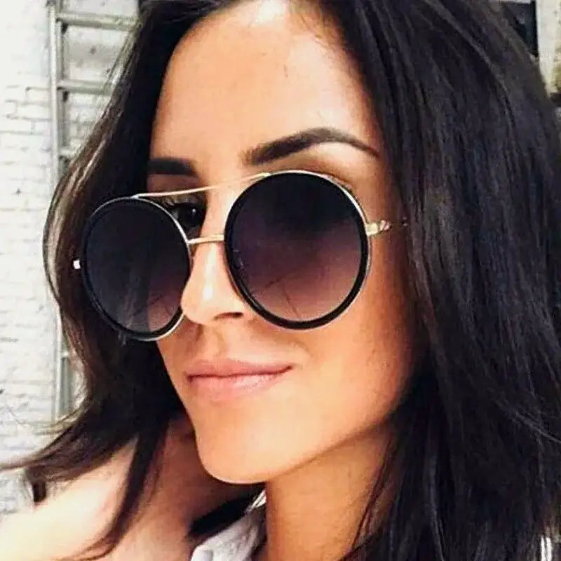 Stylish woman wearing round sunglasses with designer flair, featuring a sleek black frame and gradient lenses