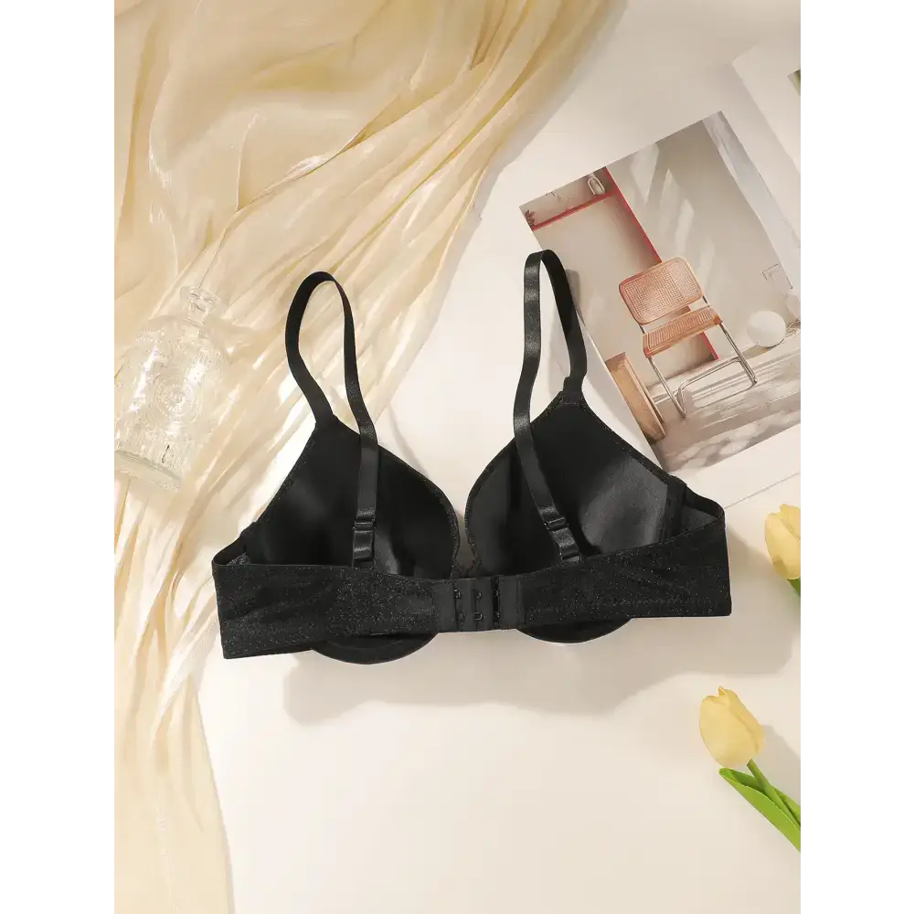Black sequin lingerie bra with steel ring and adjustable straps laid on cream fabric