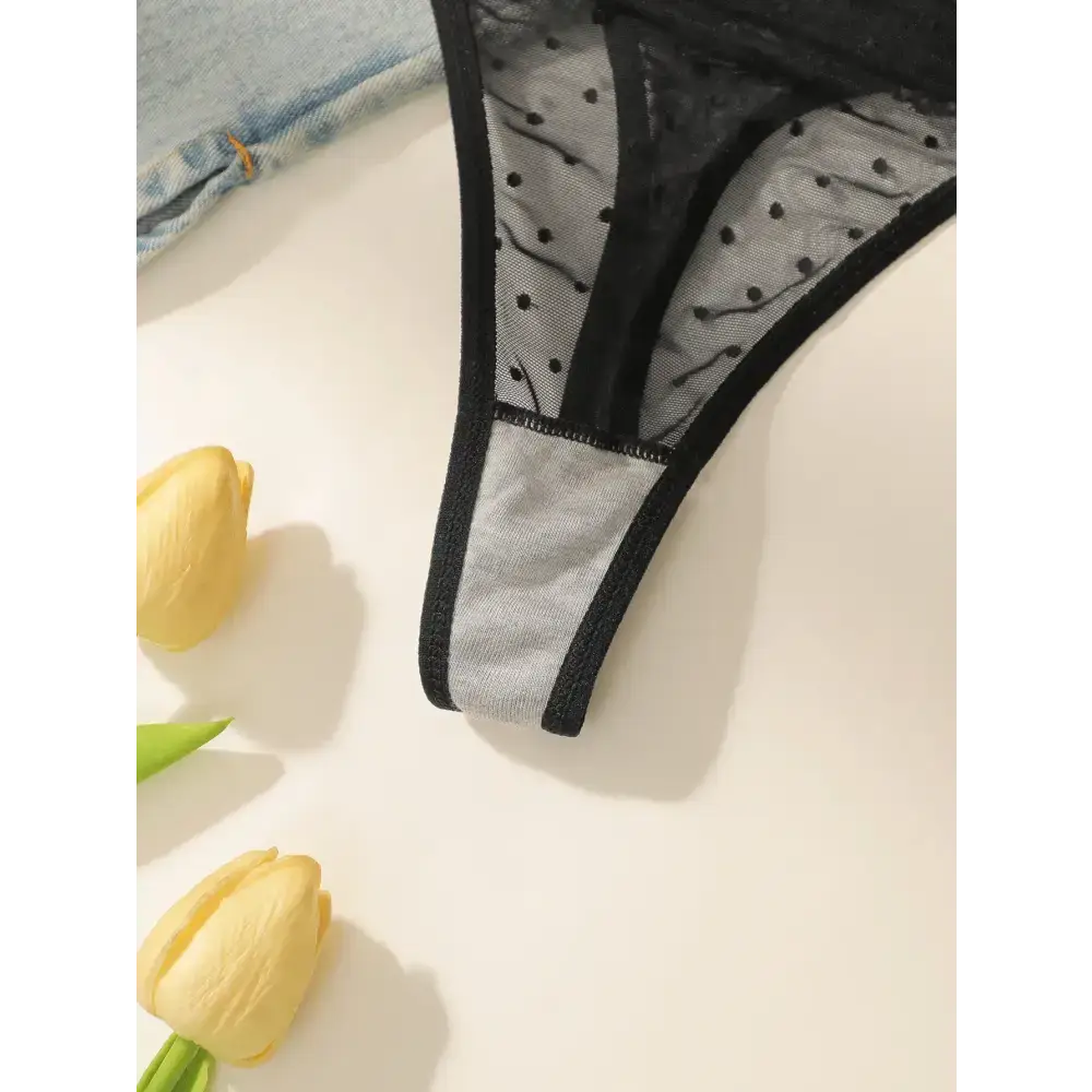 Black sexy embroidered lace lingerie set thong with polka dot mesh and solid trim laid on white surface with yellow tulips